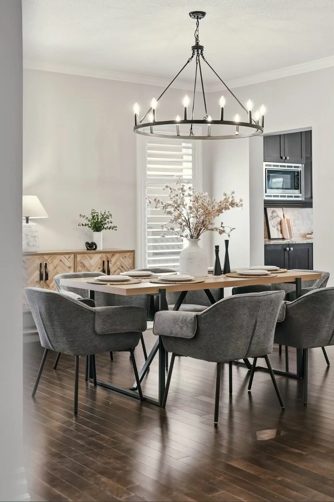 Dining room with grey upholstered chairs, a wood table and a circular chandelier