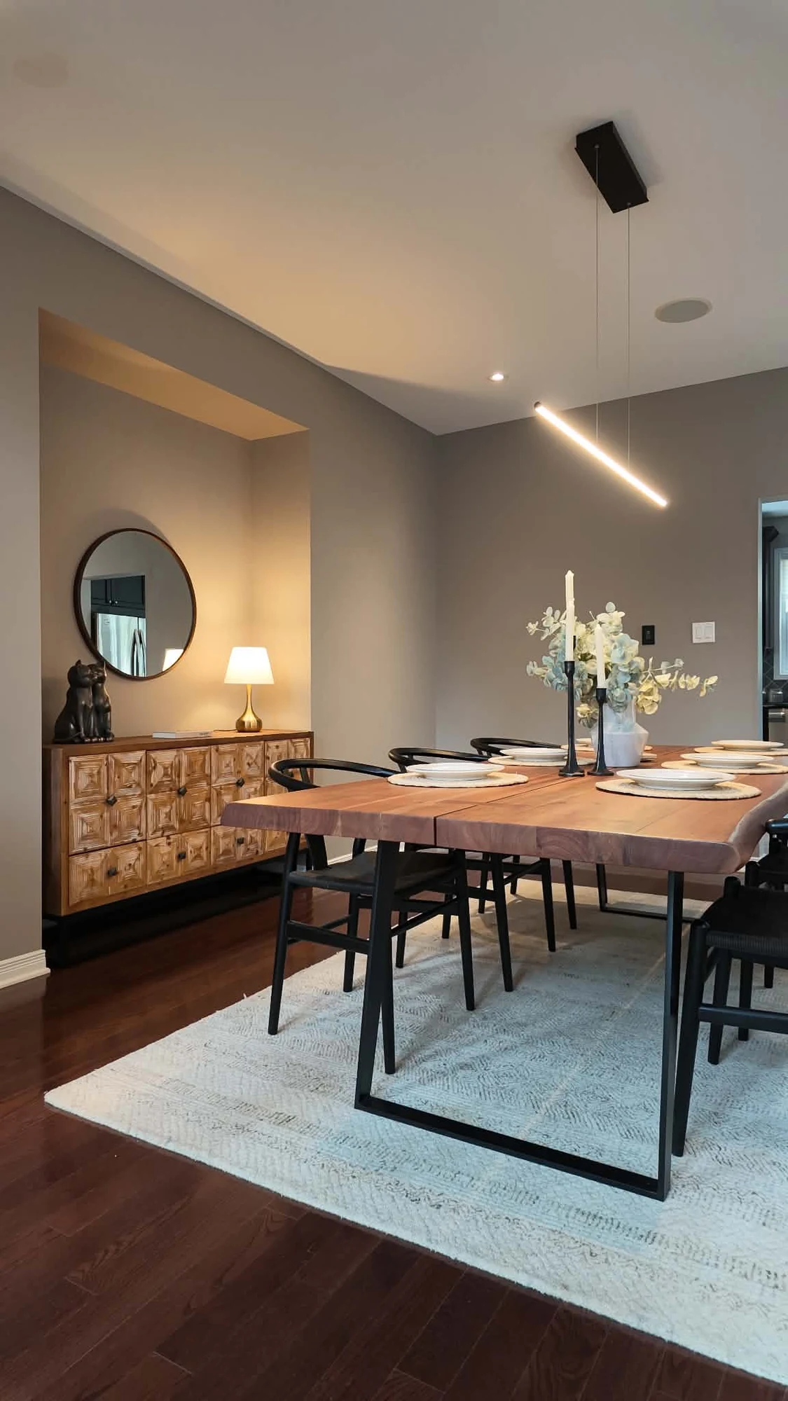 Dining room with a thick wood table, black chairs, a carved sideboard and linear pendant