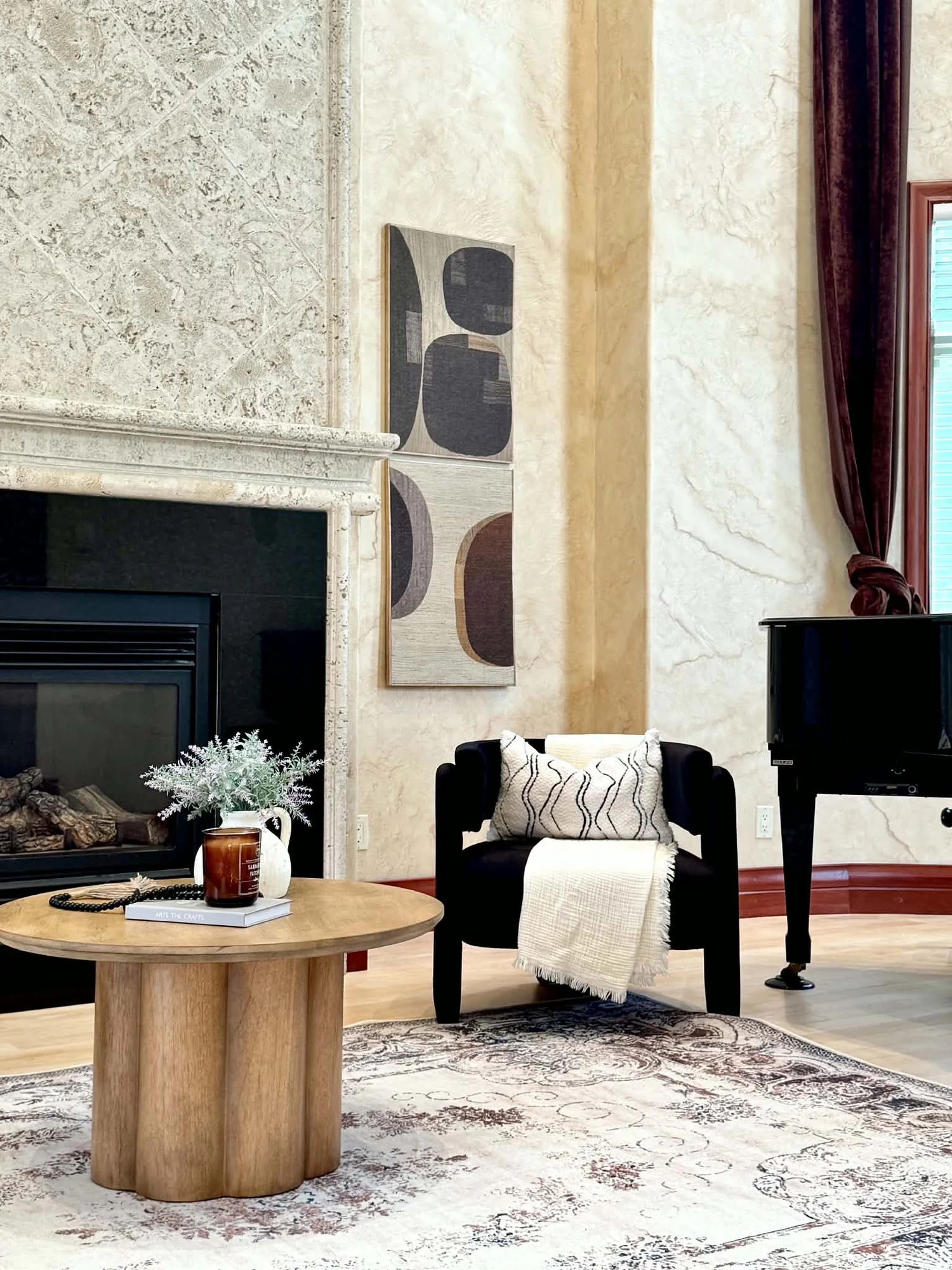 Living room with a stone fireplace, black accent chair, round wood table and grand piano